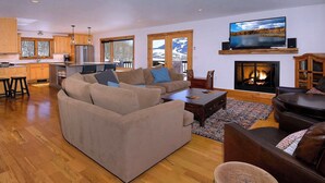 Una sala de estar moderna con un sofá grande, una chimenea, un televisor y una cocina al fondo.