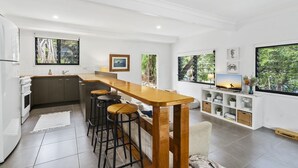 Una cocina moderna con una barra de madera, taburetes de bar, un televisor y un ventanal con vistas a árboles.
