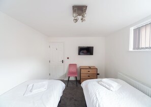 A bedroom with two beds, a dresser, a chair, a television, and a radiator. - Lovely 3 bedroom serviced apartment in Morecambe. (Morecambe)