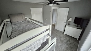 A bedroom with a bunk bed, a desk with a lamp, a television, and two doors.