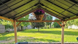 A covered patio area with wicker furniture, a hanging flower basket, and a view of a grassy yard. - Large Private Yard, 4br home, Walk to town center (Meredith)