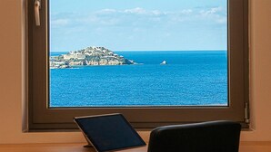 Uitzicht vanuit een raam, met een tablet op een bureau, op een kustgebied met gebouwen op een klein eiland en een boot in het water.