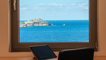 A view from a window with a tablet on a desk, overlooking a coastal area with buildings on a small island and a boat in the water.