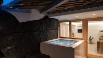 Ein moderner Wellnessbereich mit Whirlpool, Steinwand und Holzboden.