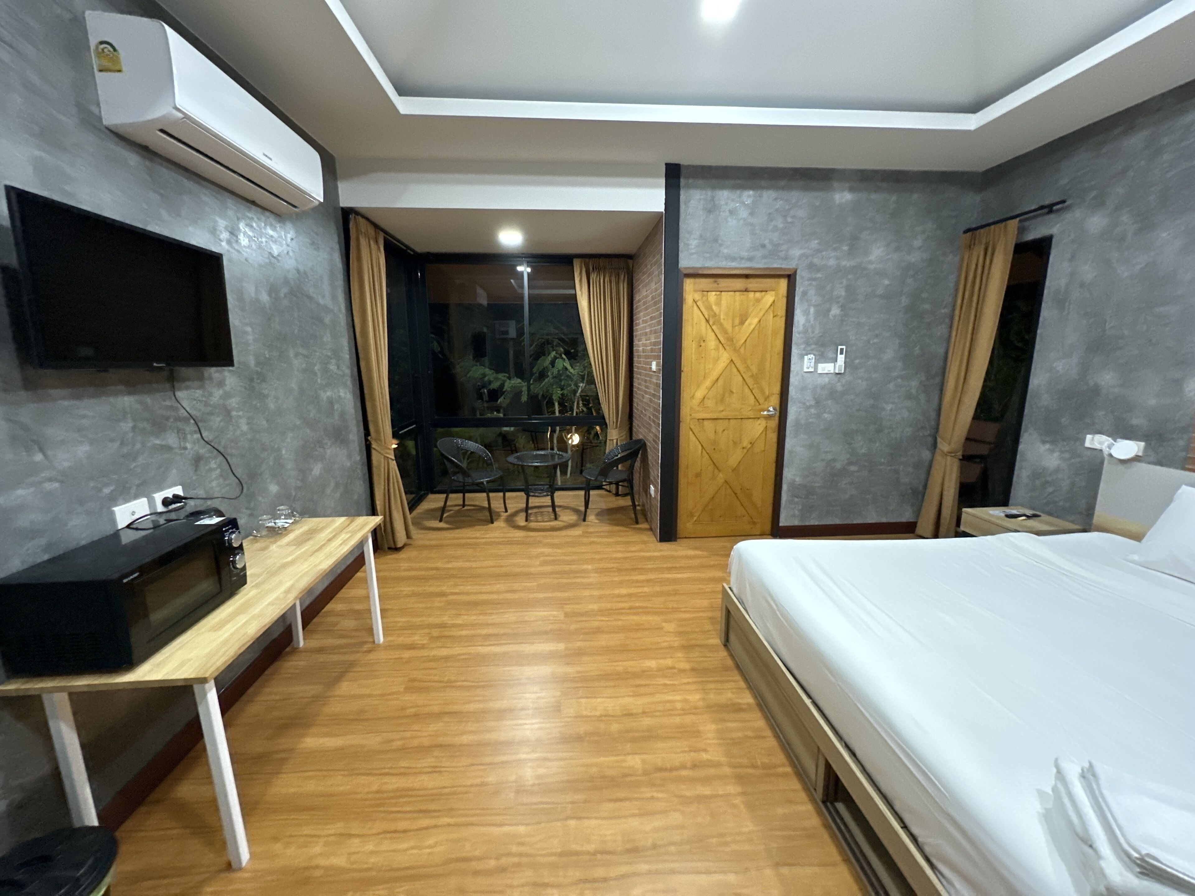 A hotel room with a bed, a desk with a computer, a TV, and a balcony with a table and chairs.