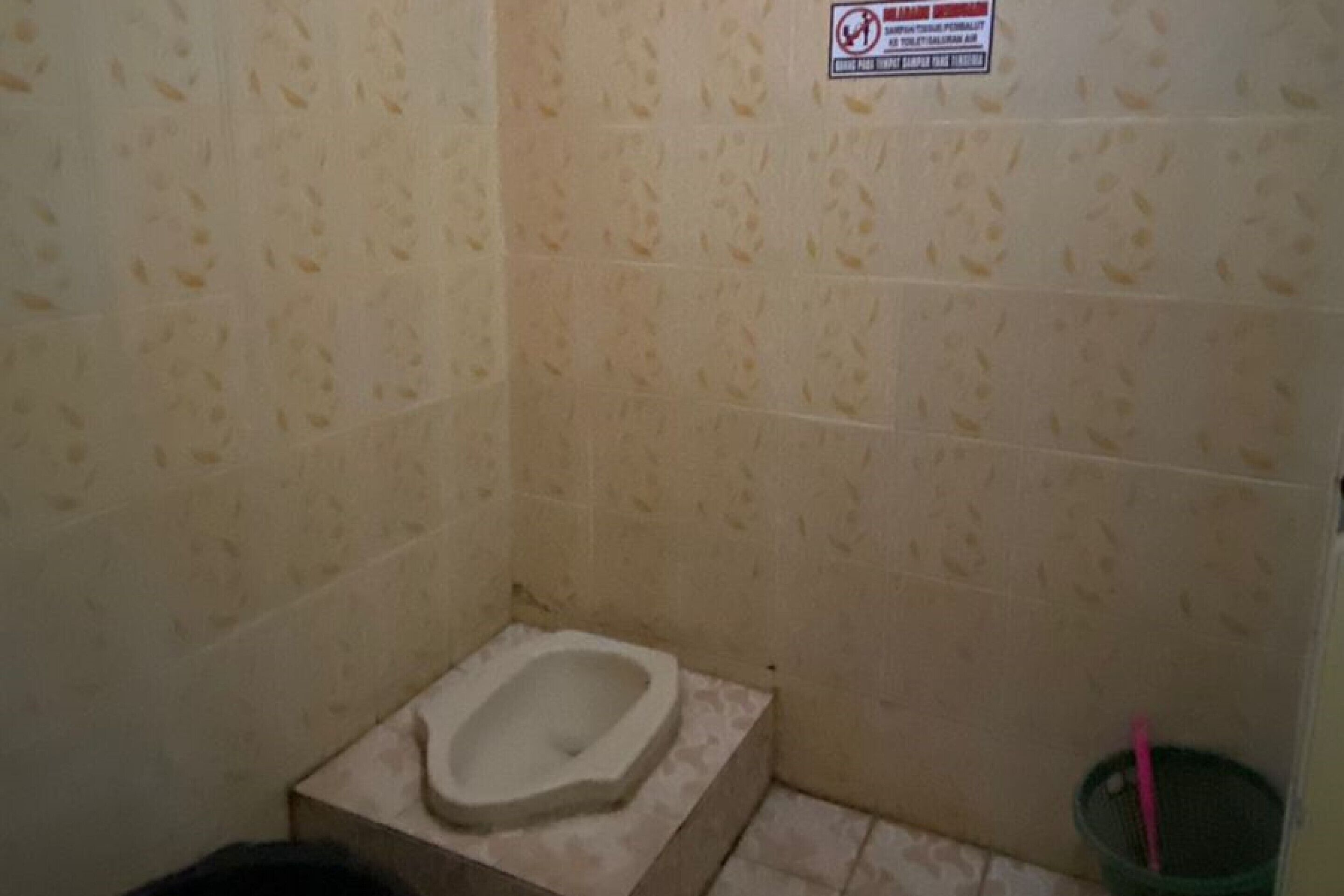 A small bathroom with a toilet, a trash bin, and a sign on the wall.