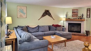 Un salon comprenant un canapé d’angle, une table basse en bois, une cheminée et une carte accrochée au mur.