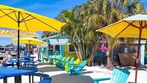 Een café aan het strand met terras, inclusief tafels en stoelen, onder gele parasols.