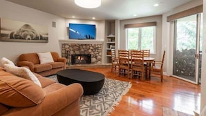 Una sala de estar con chimenea, televisor, sofá, mesa de comedor con sillas y un ventanal grande.