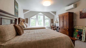 Un dormitorio con una cama grande, un aparador de madera y un escritorio con una silla. Dos ventanas ofrecen luz natural.