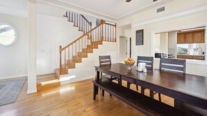 A dining area with a wooden table, benches, and a fruit bowl. A staircase with wooden railings leads to another room. - Talal R Muhtaseb (Oceanside)