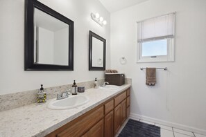 Un baño con dos lavamanos, armarios de madera, un espejo grande y una ventana con persianas.