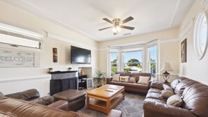 A spacious living room with leather sofas, a wooden coffee table, and a ceiling fan. A TV is mounted on the wall, and there is a fireplace with a mantel. - Talal R Muhtaseb (Oceanside)