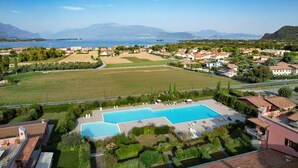 Una zona residencial con una gran piscina rodeada de casas, un campo verde y montañas al fondo.