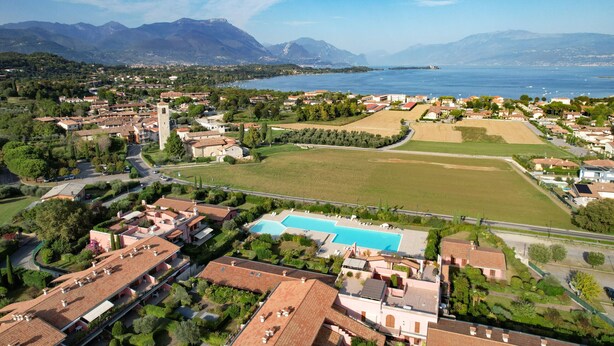 Un pueblo costero con una torre destacada, una amplia piscina y vistas al mar y las montañas.