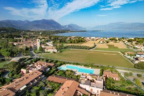 A coastal town with a prominent tower, a large swimming pool, and a view of the sea and mountains. - Apartment Aqua near to the lake and the beach (Manerba del Garda)