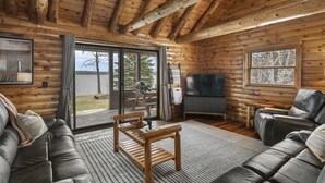 A log cabin interior with a wooden ceiling, a sofa, a coffee table, a television, and a large window.