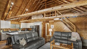 A log cabin interior with a dining area, kitchen, and two leather sofas.