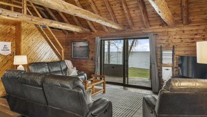 A cozy cabin with a wooden interior, leather sofas, a television, and a view of the lake.