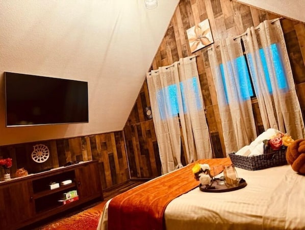 A bedroom with a TV, wooden walls, a bed, and curtains.