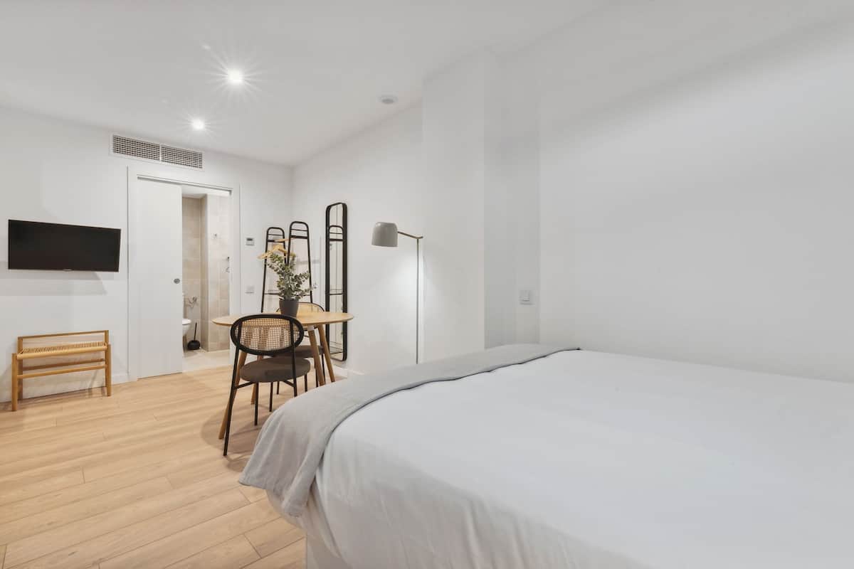 Un dormitorio moderno con una cama grande, un escritorio con silla, un televisor y una lámpara.