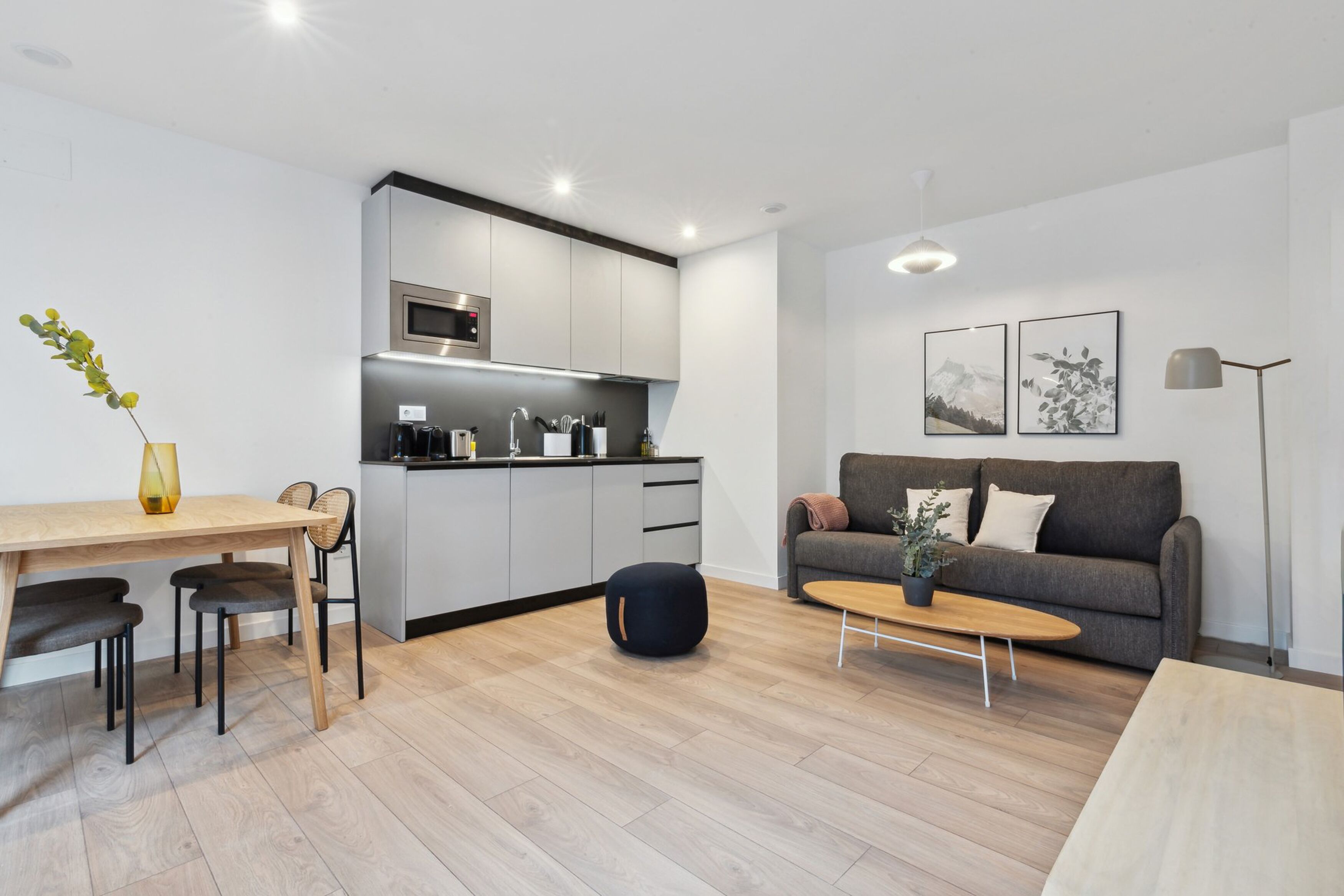 A modern kitchen with grey cabinets, a microwave, and a sink. There is a dining table with chairs and a sofa in the living area.