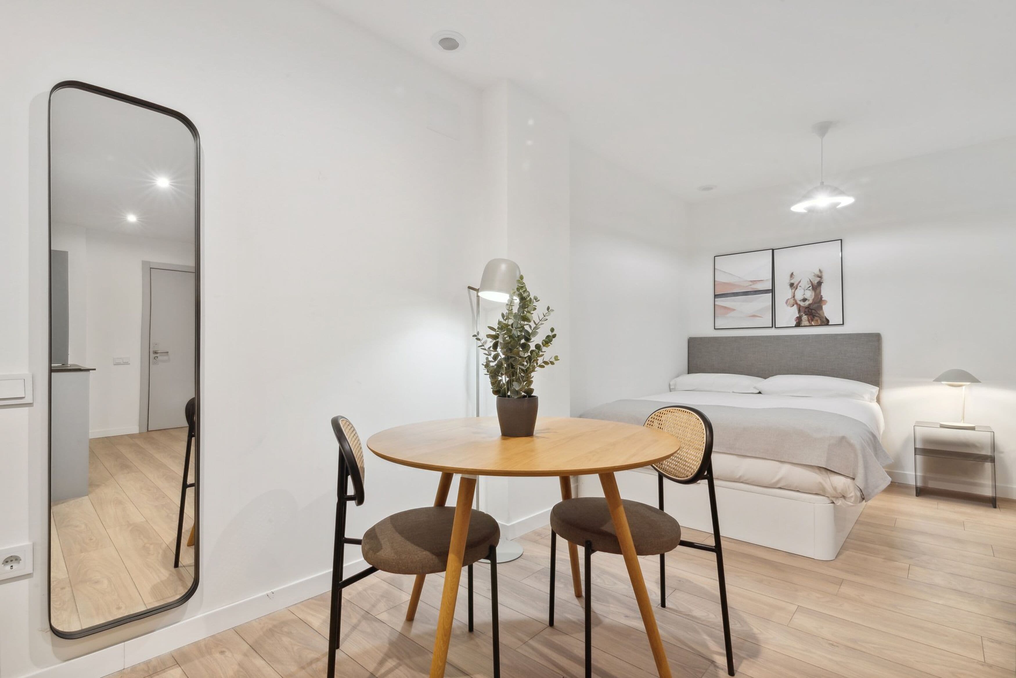 Een moderne, goed verlichte kamer met een bed, nachtkastje, lamp en een zithoek met stoelen en een tafel.