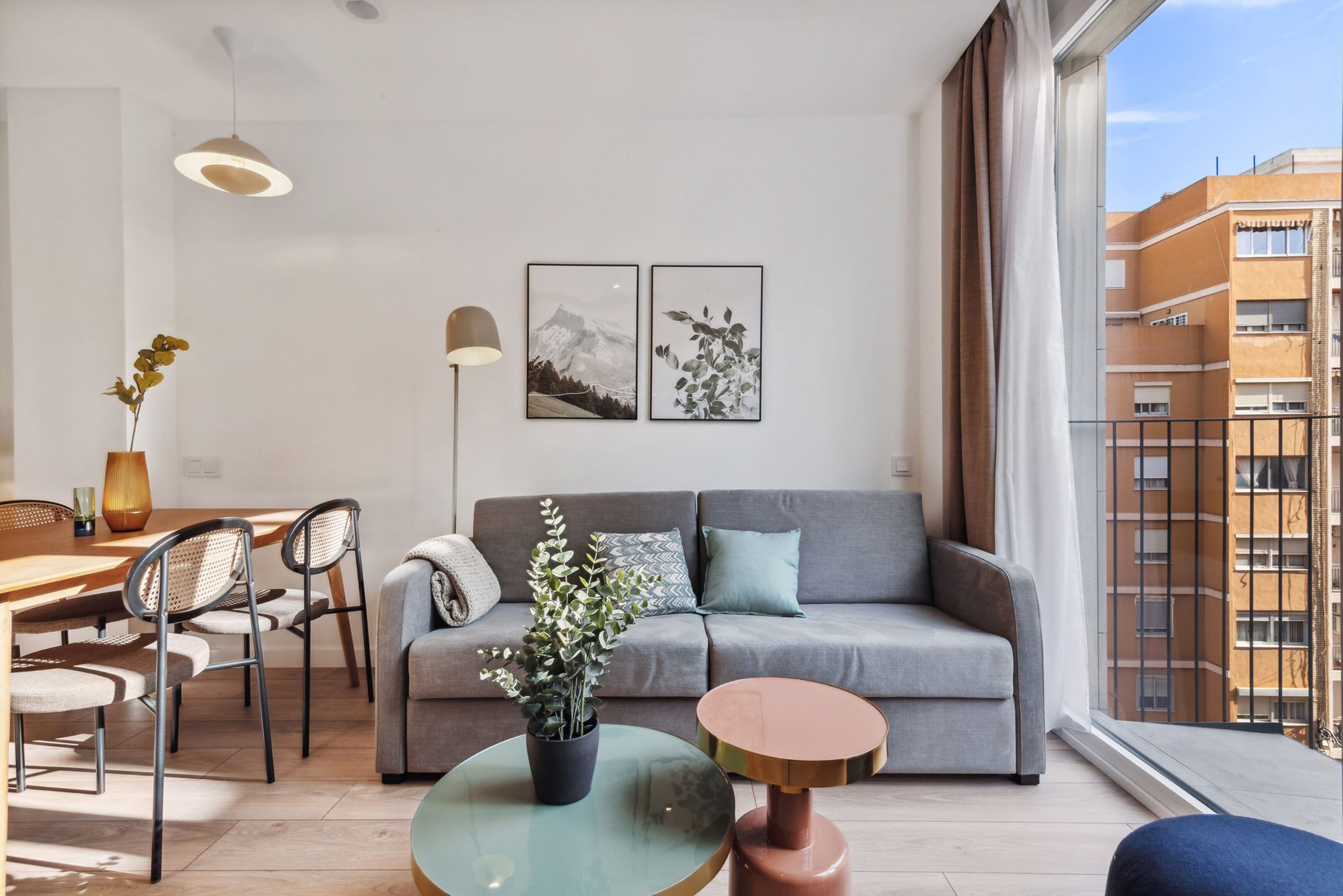 Un soggiorno moderno con un divano grigio, un tavolino da caffè in vetro rotondo e un'area pranzo con tavolo e sedie in legno.