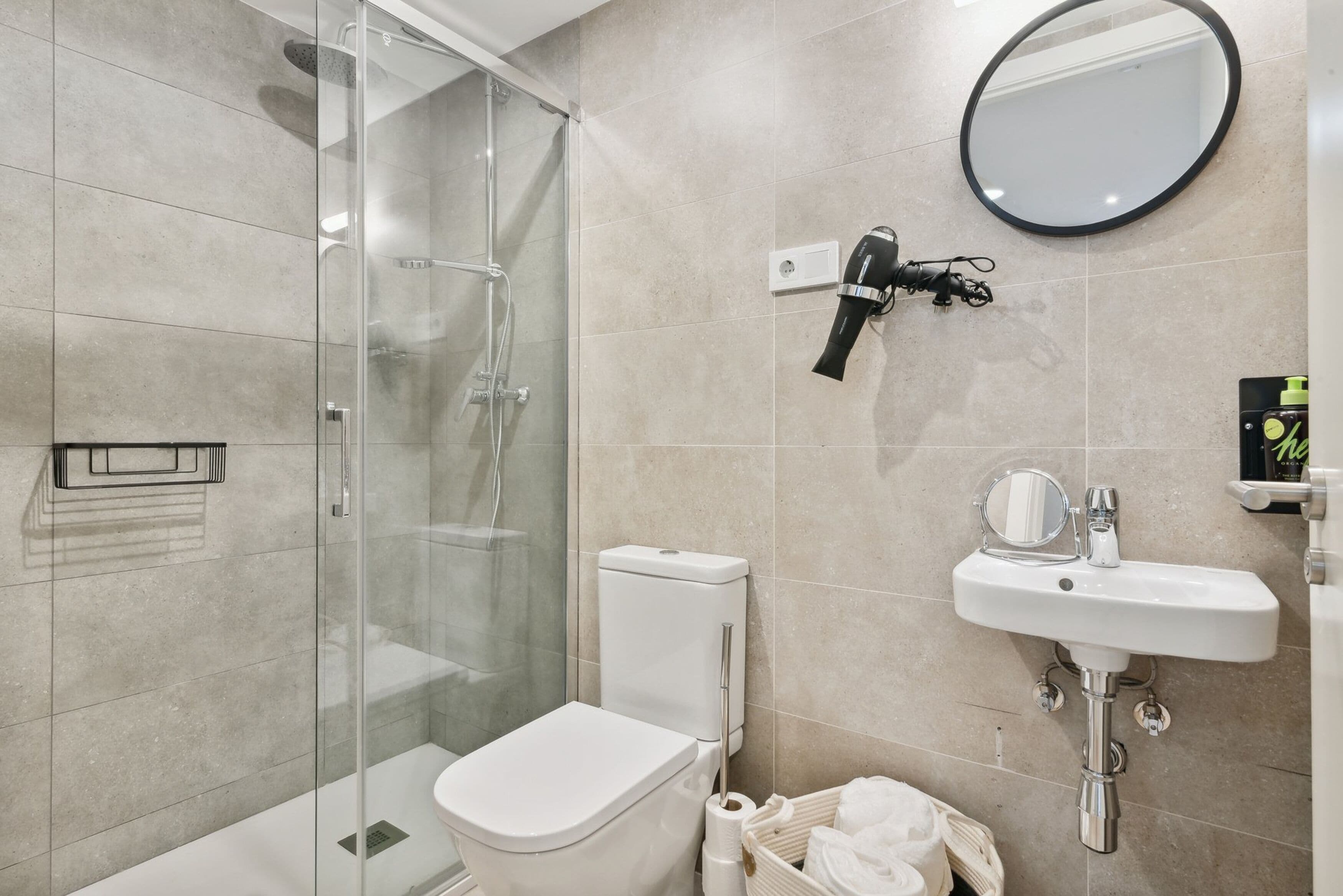 A modern bathroom with a glass-enclosed shower, a white toilet, a sink with a mirror, and a hairdryer mounted on the wall.