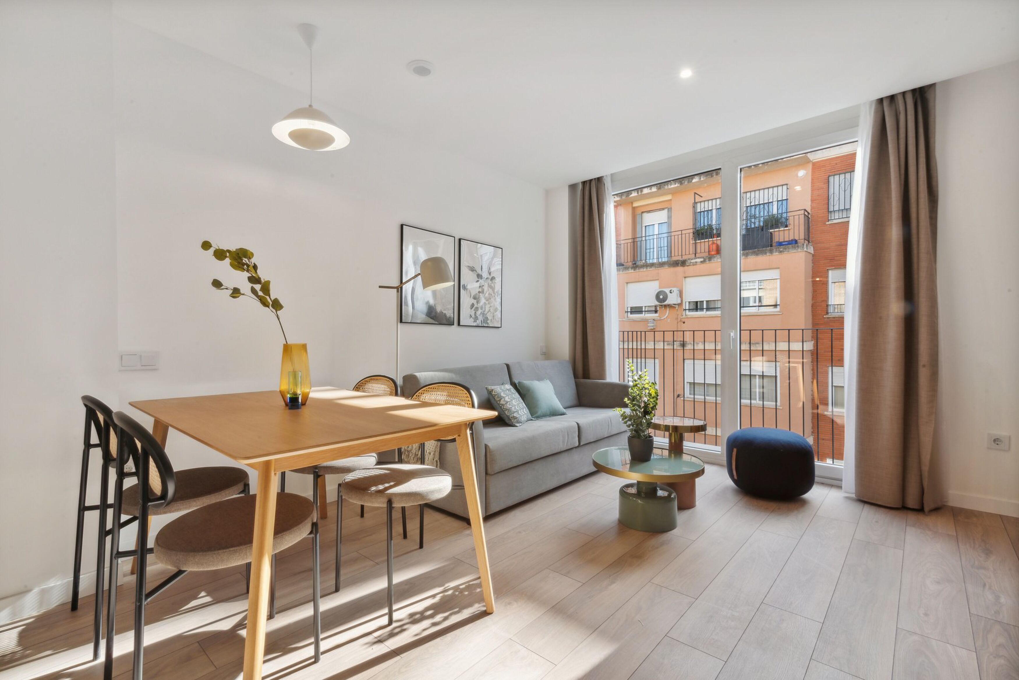 A modern living room with a dining table, sofa, and a view of a building through large windows.