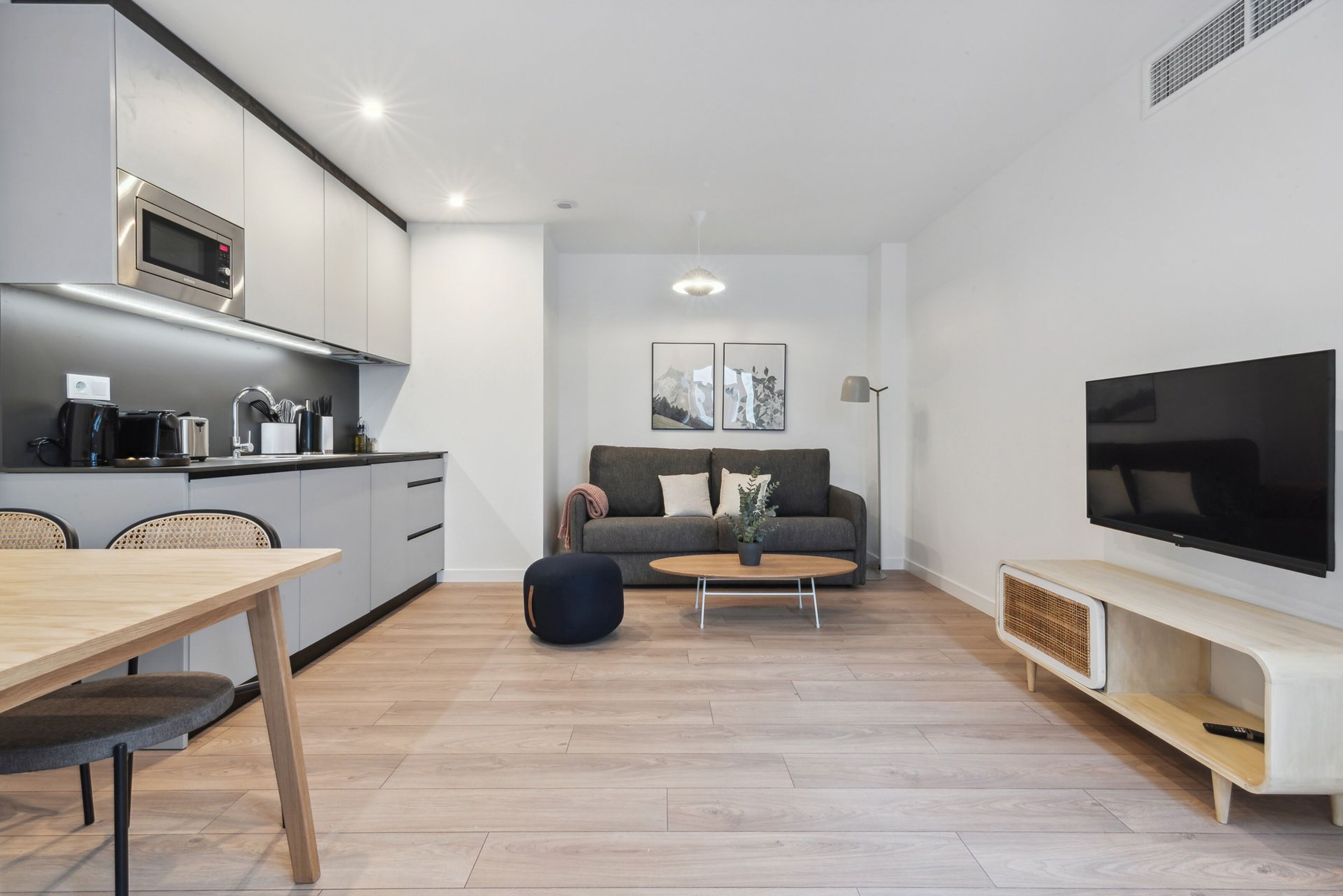Eine moderne Küche mit Mikrowelle, Esstisch und Stühlen. Ein Wohnbereich mit einer Couch, Couchtisch und einem Flachbildfernseher.