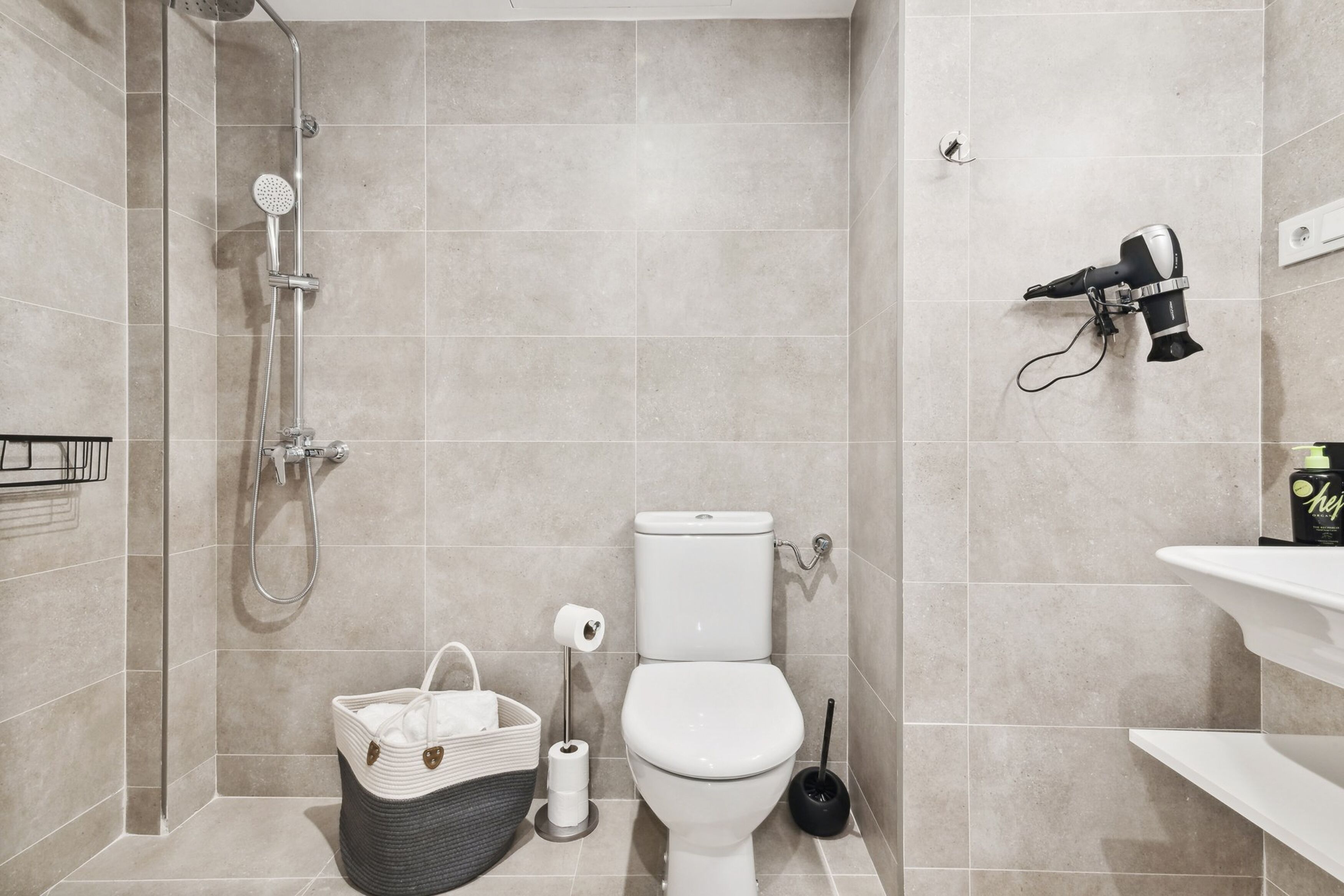 A modern bathroom with a shower, toilet, and a hairdryer mounted on the wall.