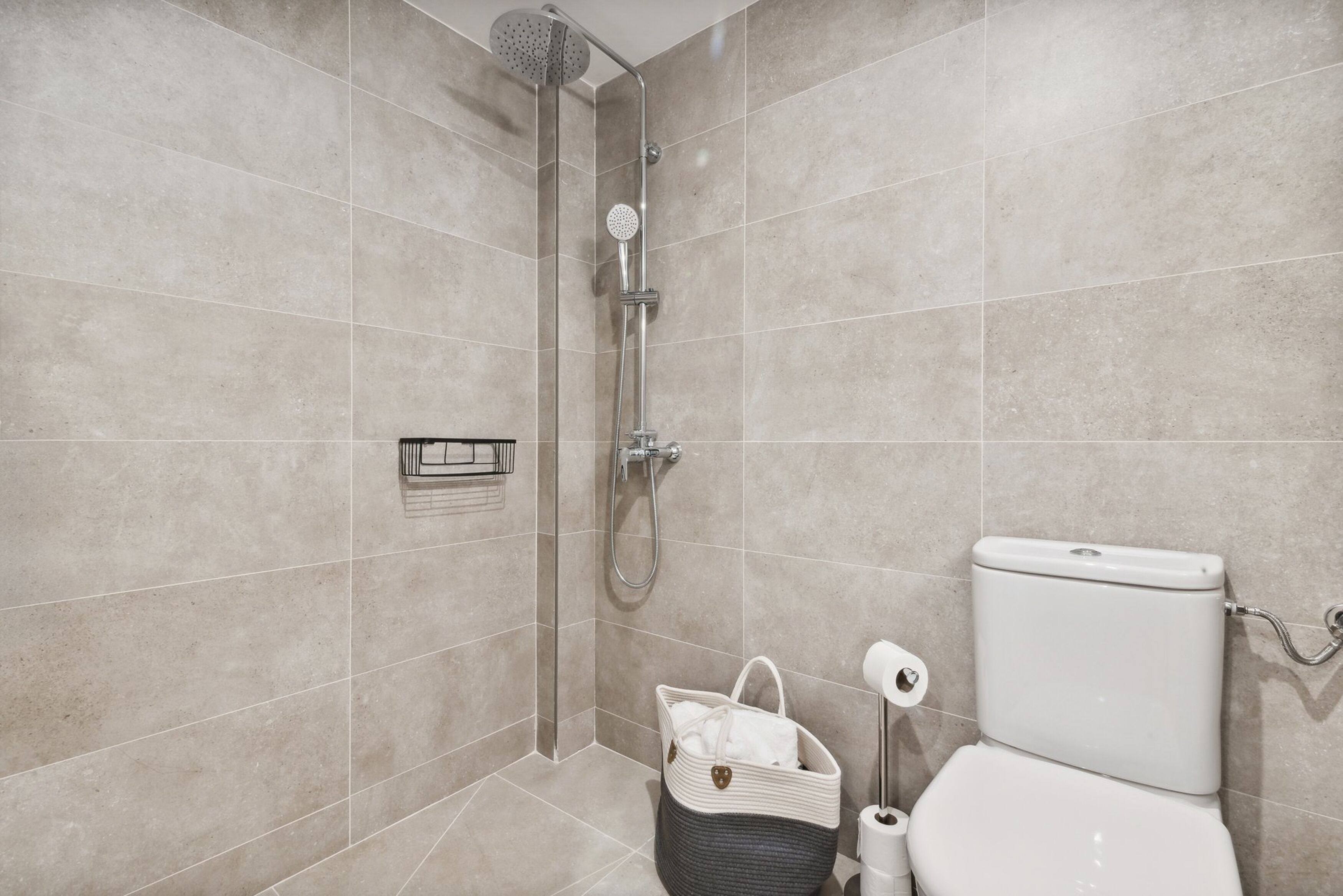 A modern bathroom with a shower, toilet, and a basket with a towel.