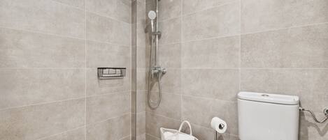 A modern bathroom with a shower, toilet, and a basket with a towel.