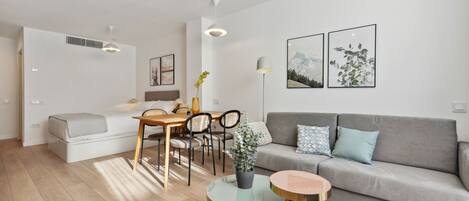 A modern living room with a grey sofa, round coffee table, and a dining area with a wooden table and chairs.