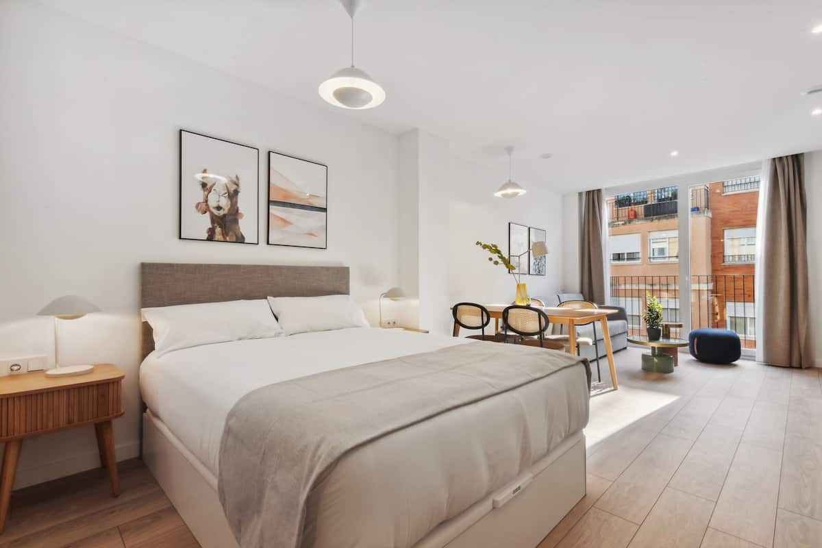 Una habitación de hotel moderna con una cama grande, un escritorio, una silla y vistas a la ciudad.