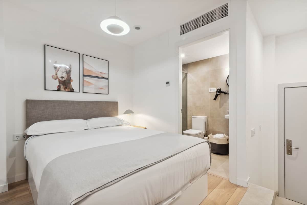 Un dormitorio moderno con una cama grande, una mesita de noche, una lámpara de pared y un cuadro enmarcado.