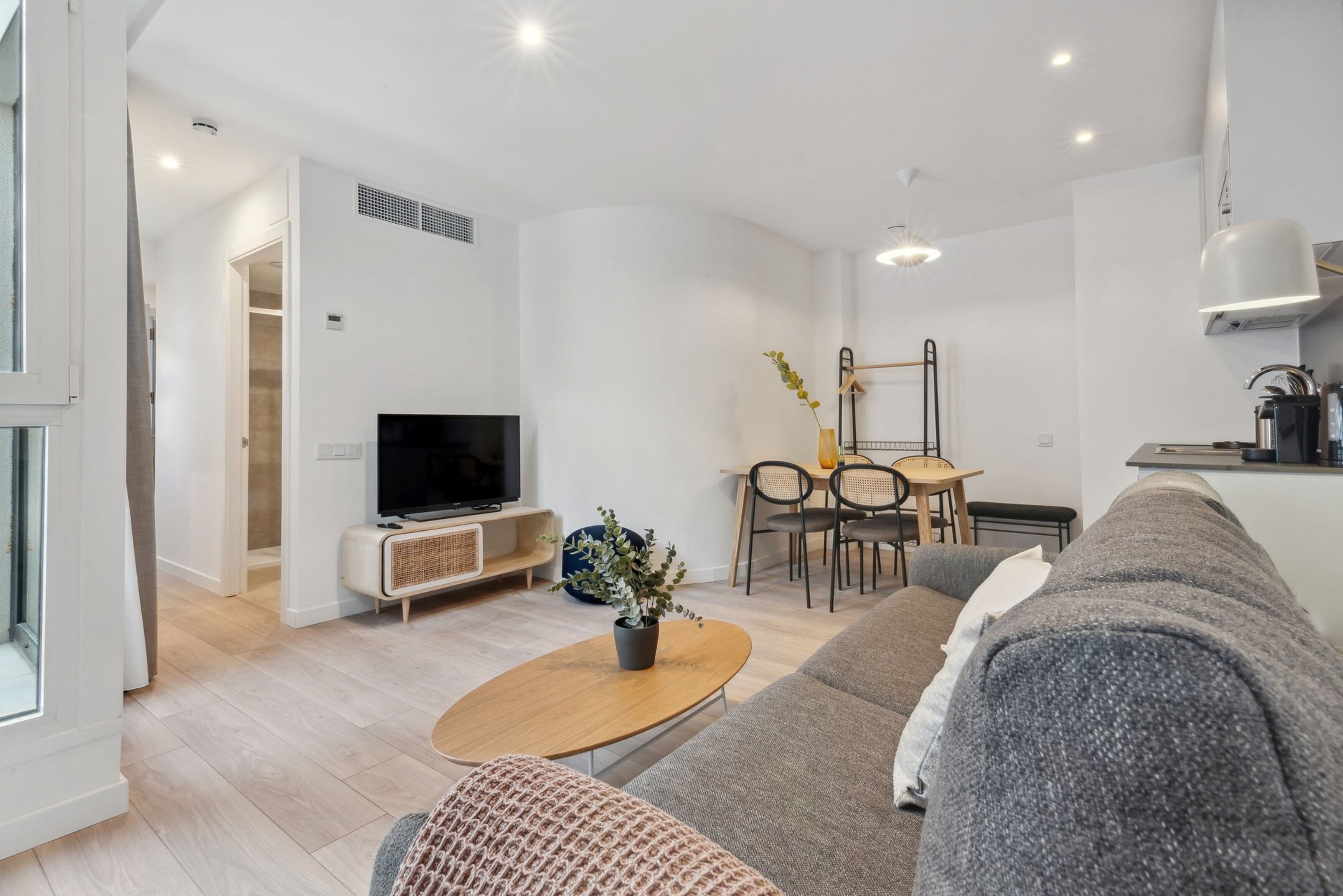 A modern living room with a sofa, a coffee table, a TV, and a dining area with chairs and a table.