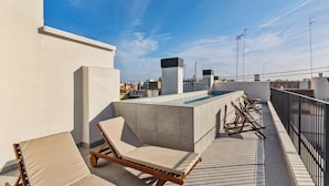 Terraza en la azotea con piscina, sillones de descanso y vistas a la ciudad.