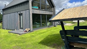 Une maison moderne à deux étages, dotée de grandes fenêtres, d’un toit en pente et d’une terrasse en bois.