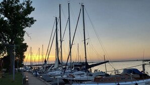 Un port de plaisance où sont amarrés plusieurs voiliers, une promenade pavée et un arbre sur la gauche.