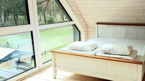 Une chambre à coucher avec un lit en bois, de grandes fenêtres et une vue sur un espace verdoyant.