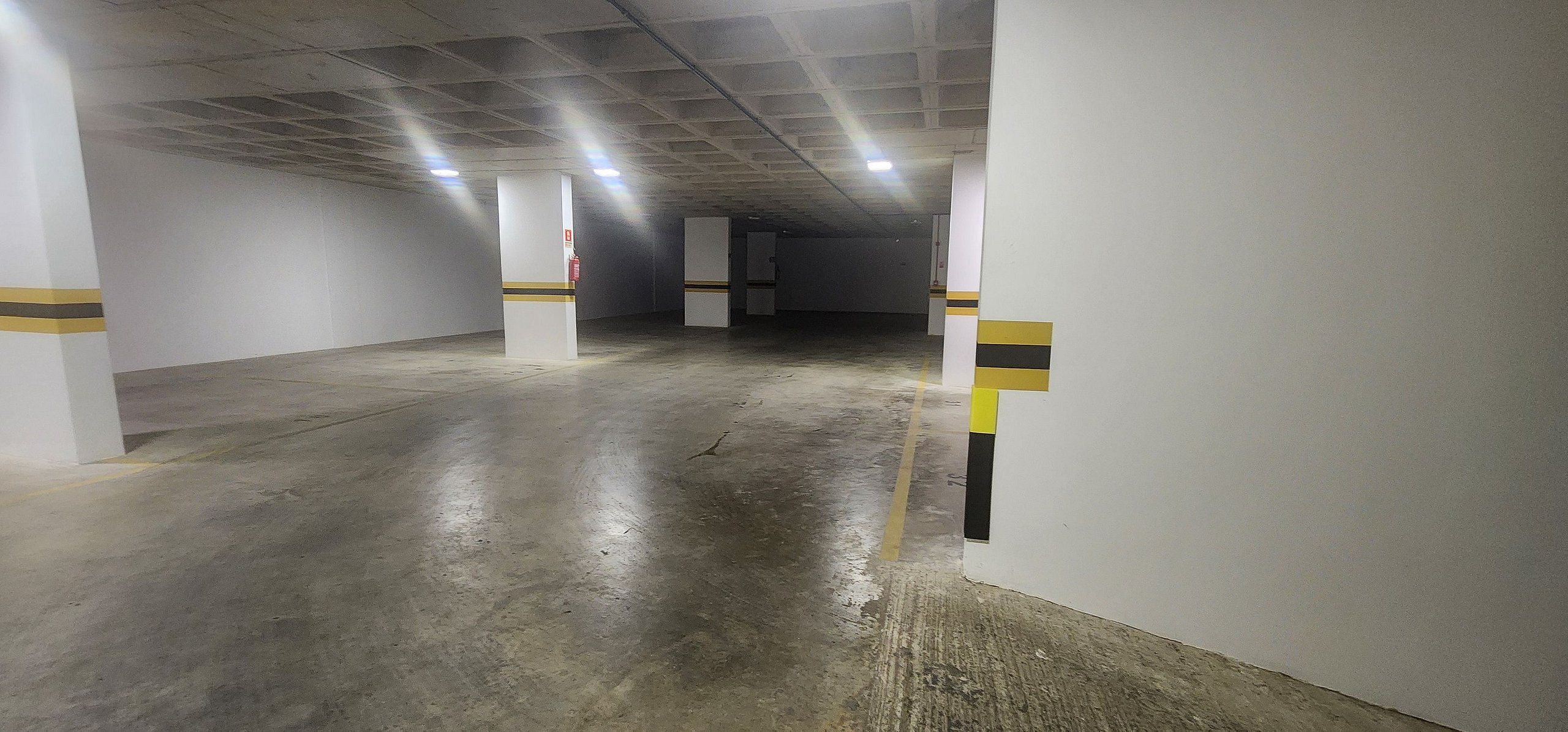 A parking garage with concrete floors and white walls, featuring yellow and black striped columns.