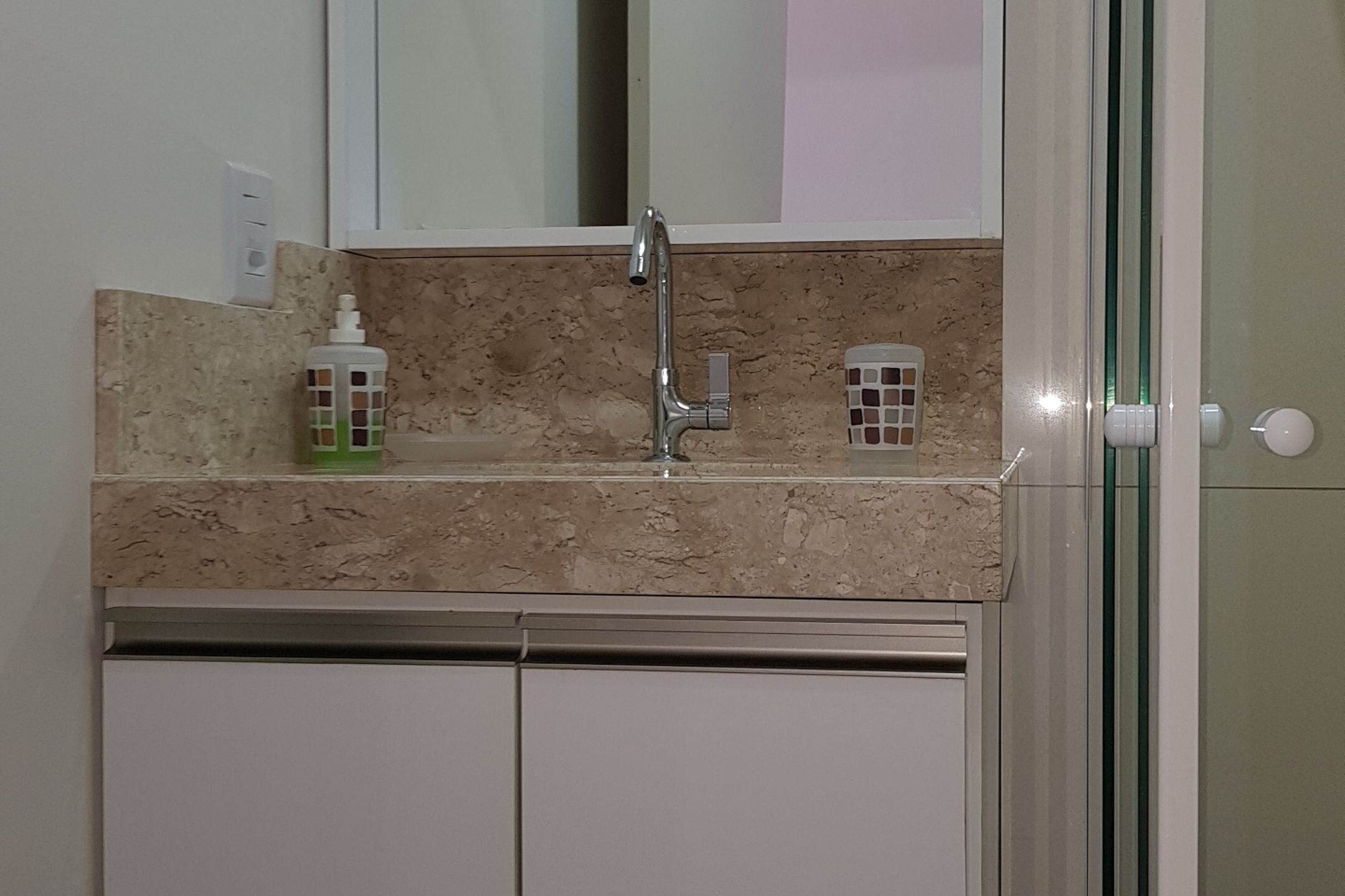 A bathroom with a marble countertop, a sink, and two soap dispensers.