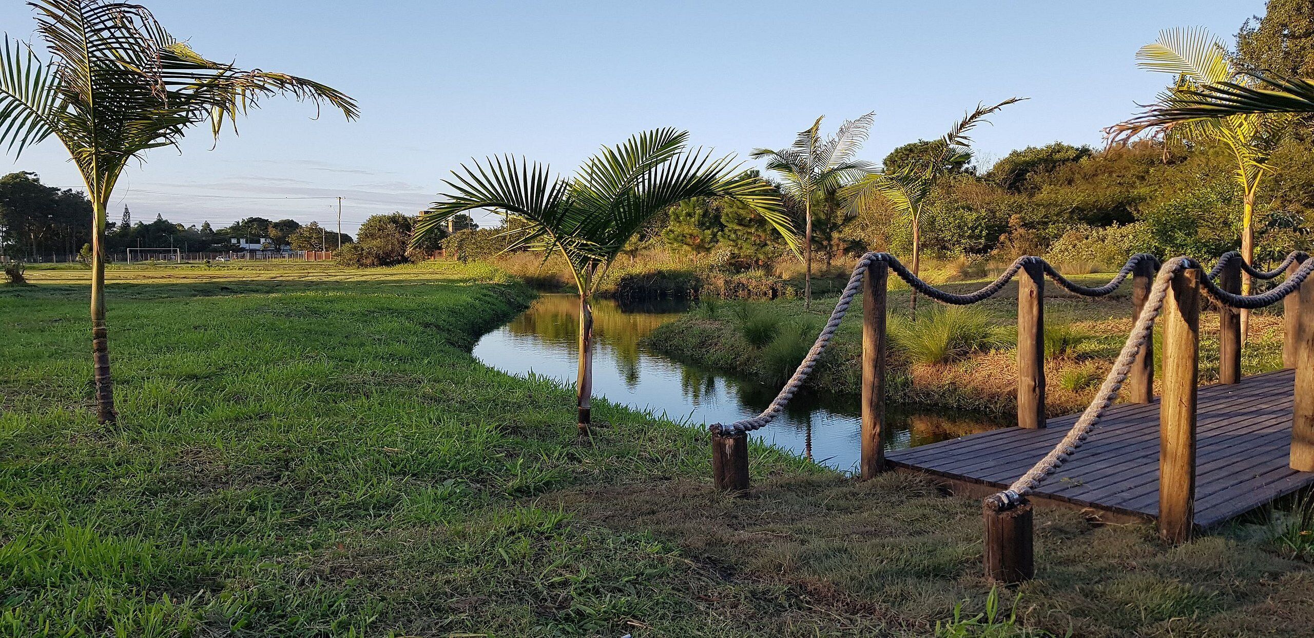 Una terraza de madera con barandillas de cuerda, un área con césped y una masa de agua.