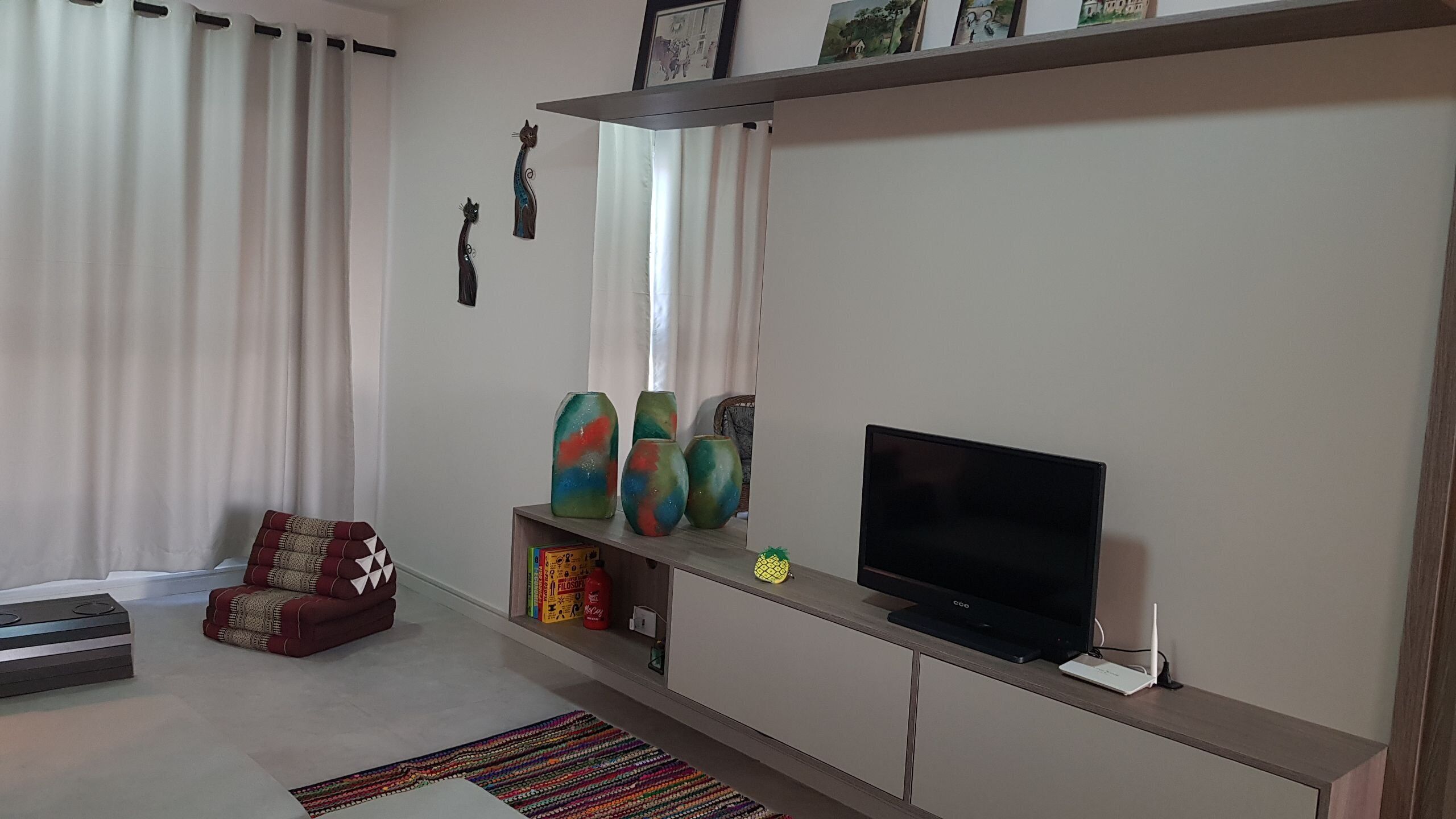 Uma sala de estar moderna com uma televisão de tela plana, vasos coloridos e um sofá vermelho estampado.