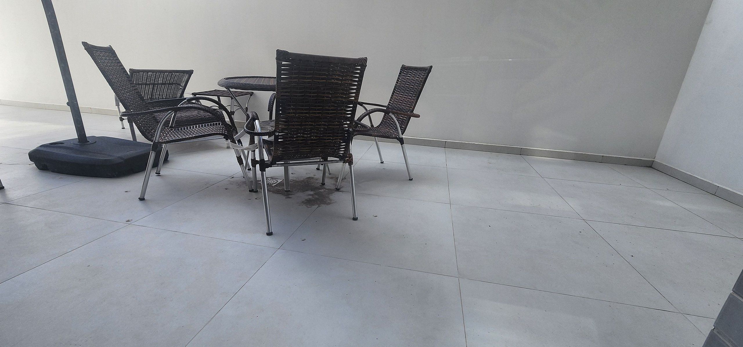 A set of four wicker chairs and a small round table on a tiled floor, with a wall in the background.