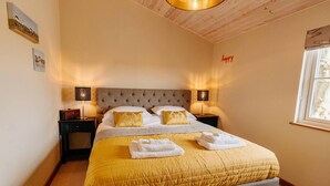 Een net opgemaakt bed met een gele sprei, twee bedlampen en een raam met uitzicht.