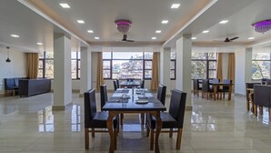 A spacious dining area with a long table, chairs, and a view of a mountainous landscape through large windows. - Treebo Stotrak S N Residency, Mussoorie (Dehradun)