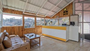 A reception area with a wooden interior, a reception desk, a seating area with a sofa, and a view of the city through large windows. - Treebo Stotrak S N Residency, Mussoorie (Dehradun)